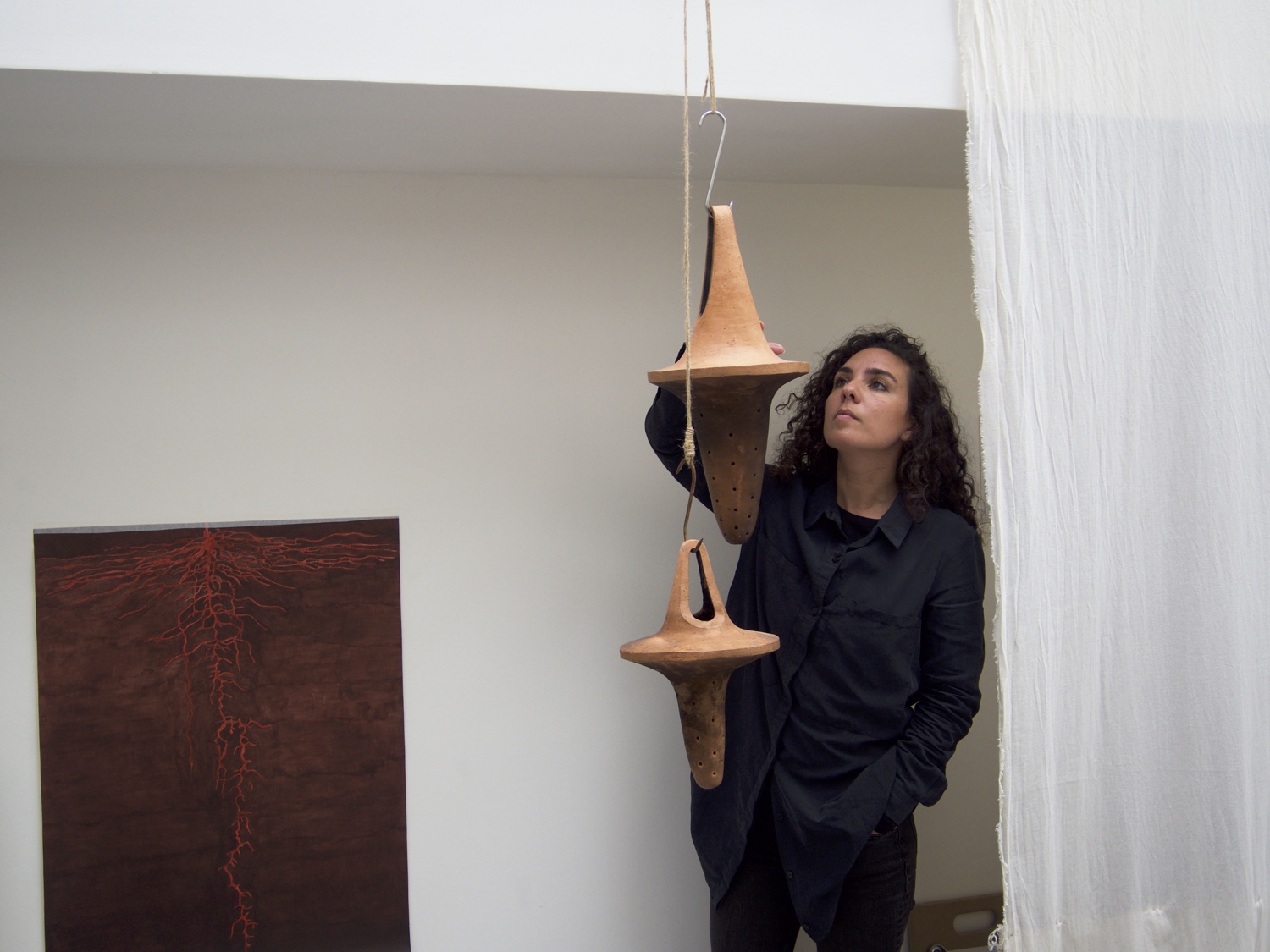 Camila Jordan at exhibition with hanging terracotta sculptures, Paris
