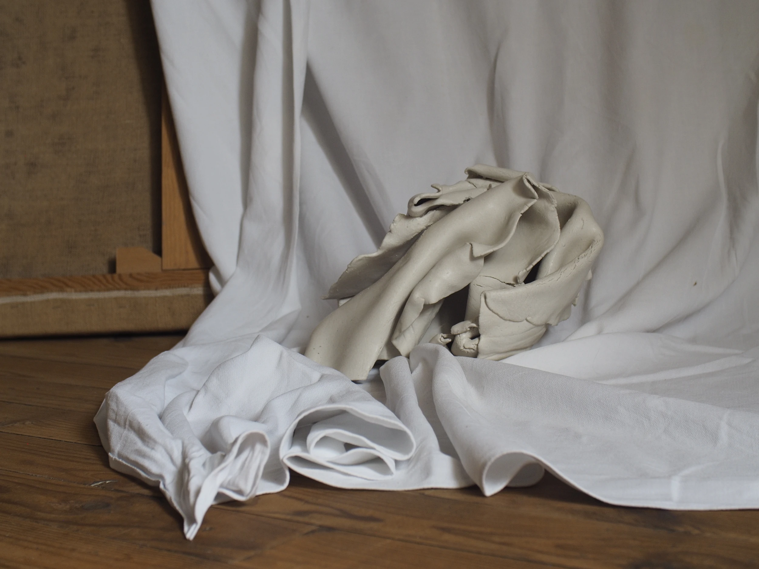 Raw clay form resting on white textile draped over a wooden studio floor