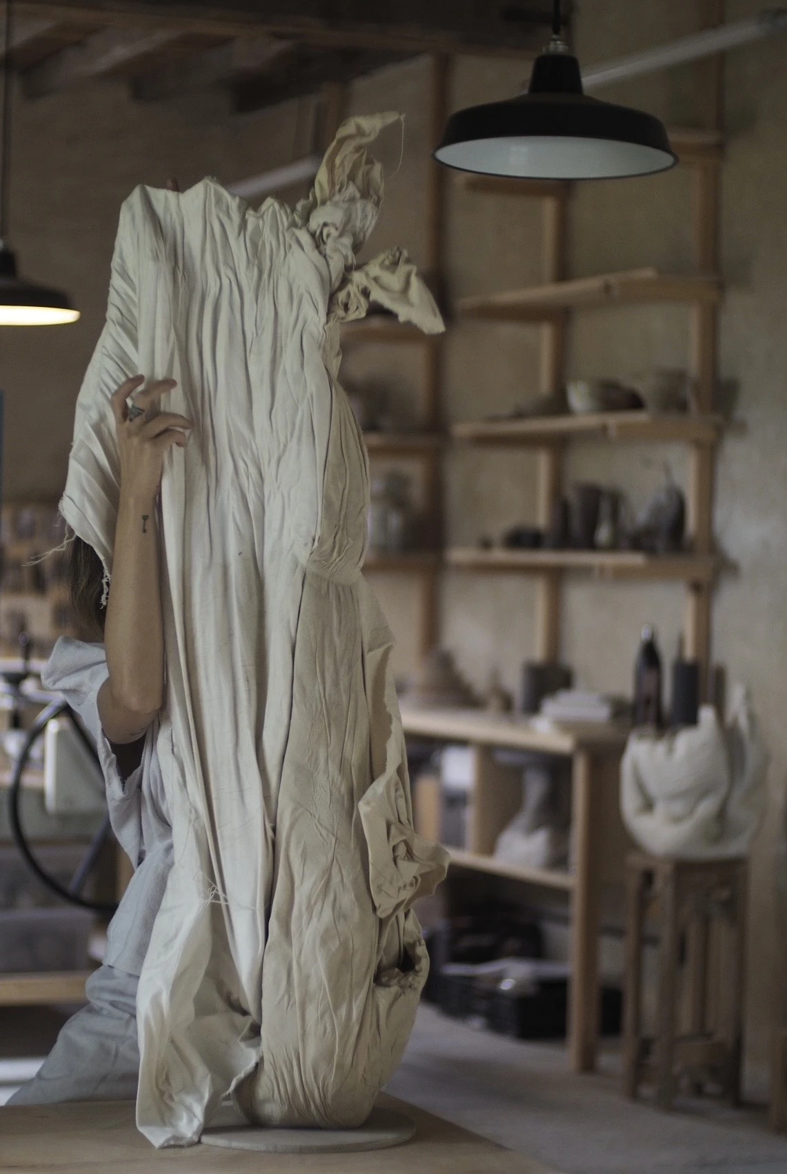 Johanna Meyer lifting the textile wrapping off a tall ceramic piece in her studio