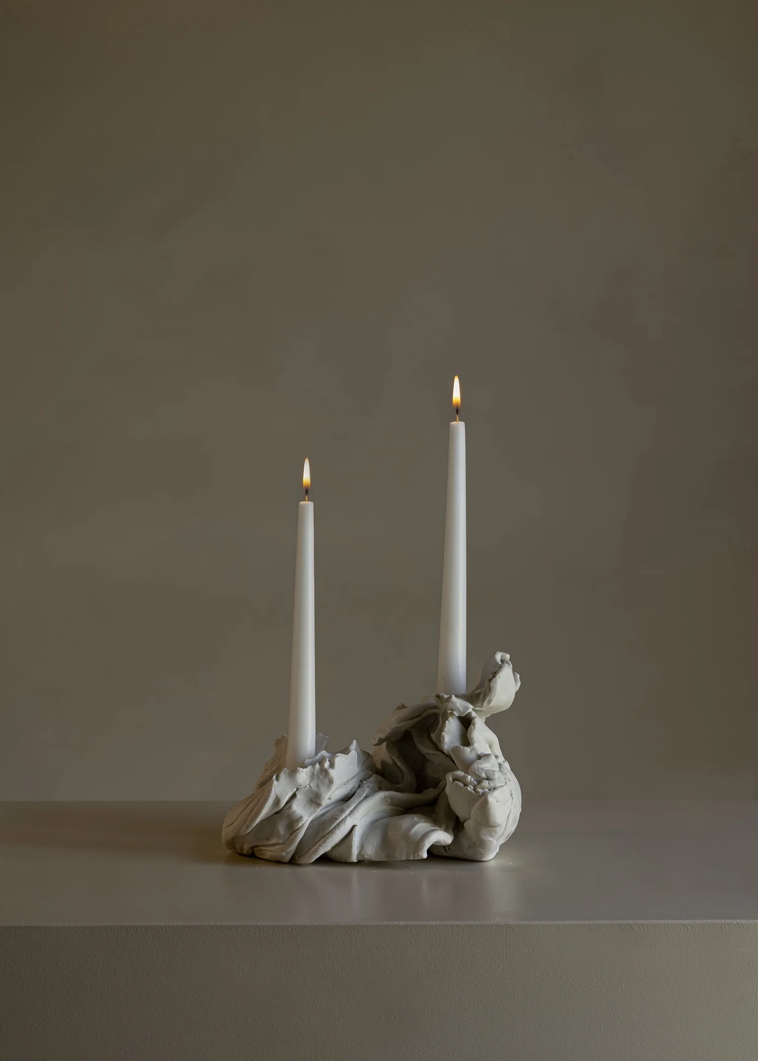 Porcelain candleholder with two lit candles against a taupe background