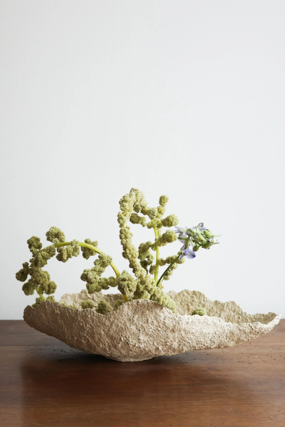 Textured ceramic vessel with green and blue ikebana flower arrangement